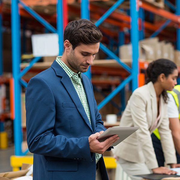 Project manager standing in front of a warehouse setting, using a tablet